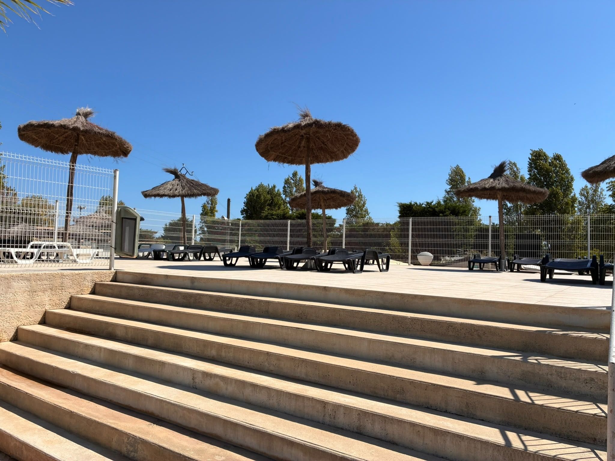 Des marches extérieures mènent à un espace aménagé avec des parasols en chaume et une clôture en métal.