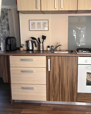 A kitchen with wooden cabinets, a coffee maker, a kettle, a sink, and a stove.