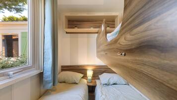 Une chambre avec deux lits, une fenêtre avec des rideaux, une table de chevet avec une lampe et une tête de lit en bois.