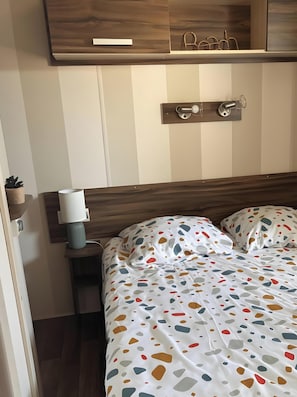 A bedroom with a bed, bedside table, lamp, and a small potted plant. - Mobile Home for 6 near Sète & Montpellier in 4-Star Campsite (Vic-la-Gardiole)
