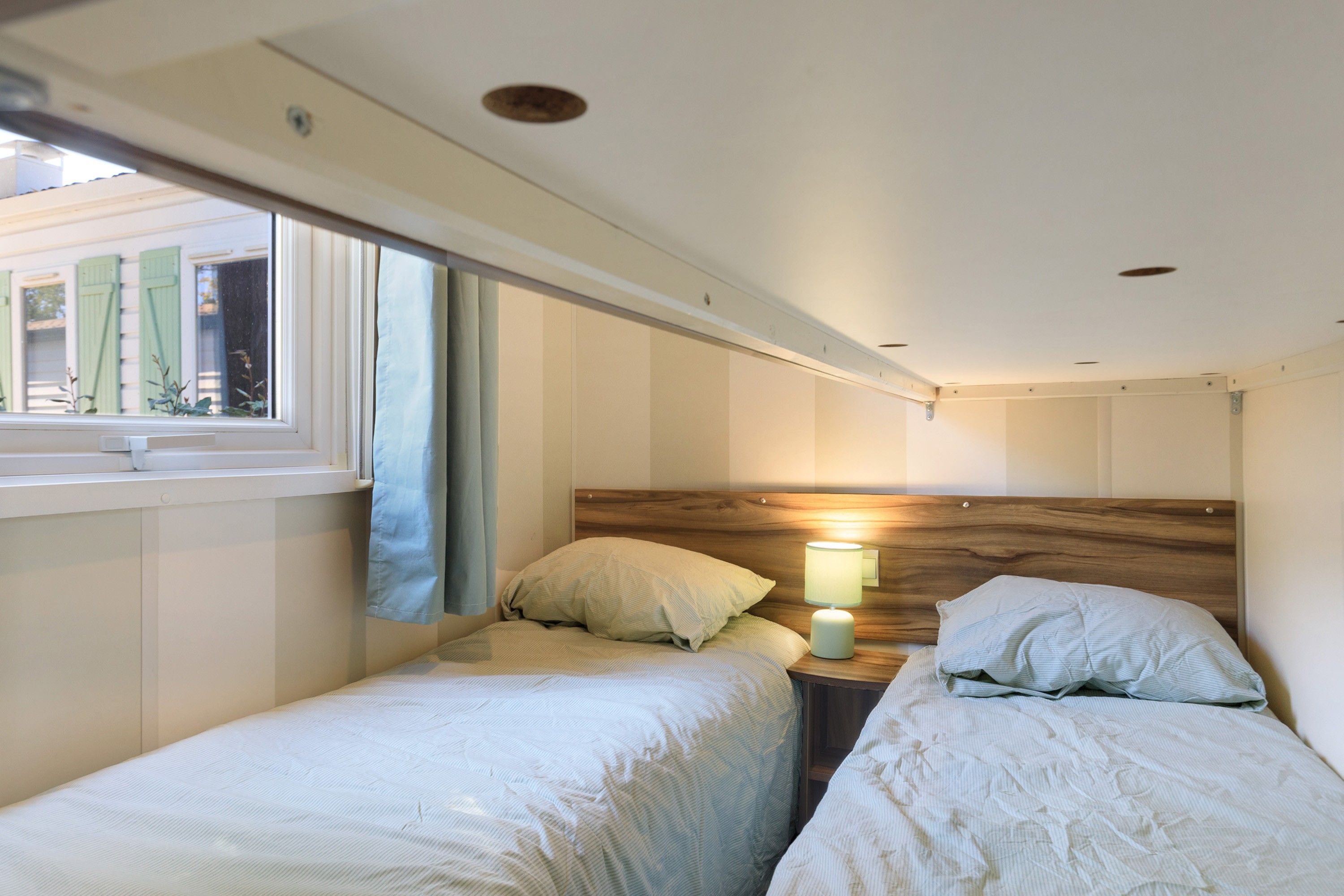 Une chambre avec deux lits simples, une table de chevet avec une lampe et une fenêtre avec des rideaux.