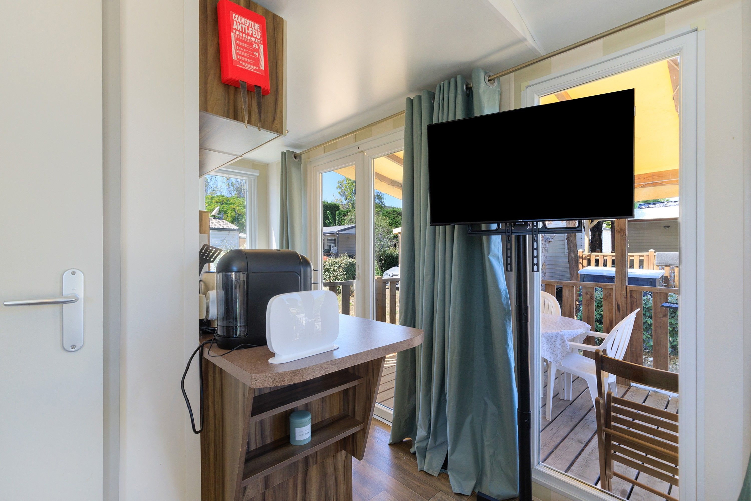 Une chambre avec un téléviseur fixé au mur, une table avec une bouilloire et une vue sur une terrasse extérieure.
