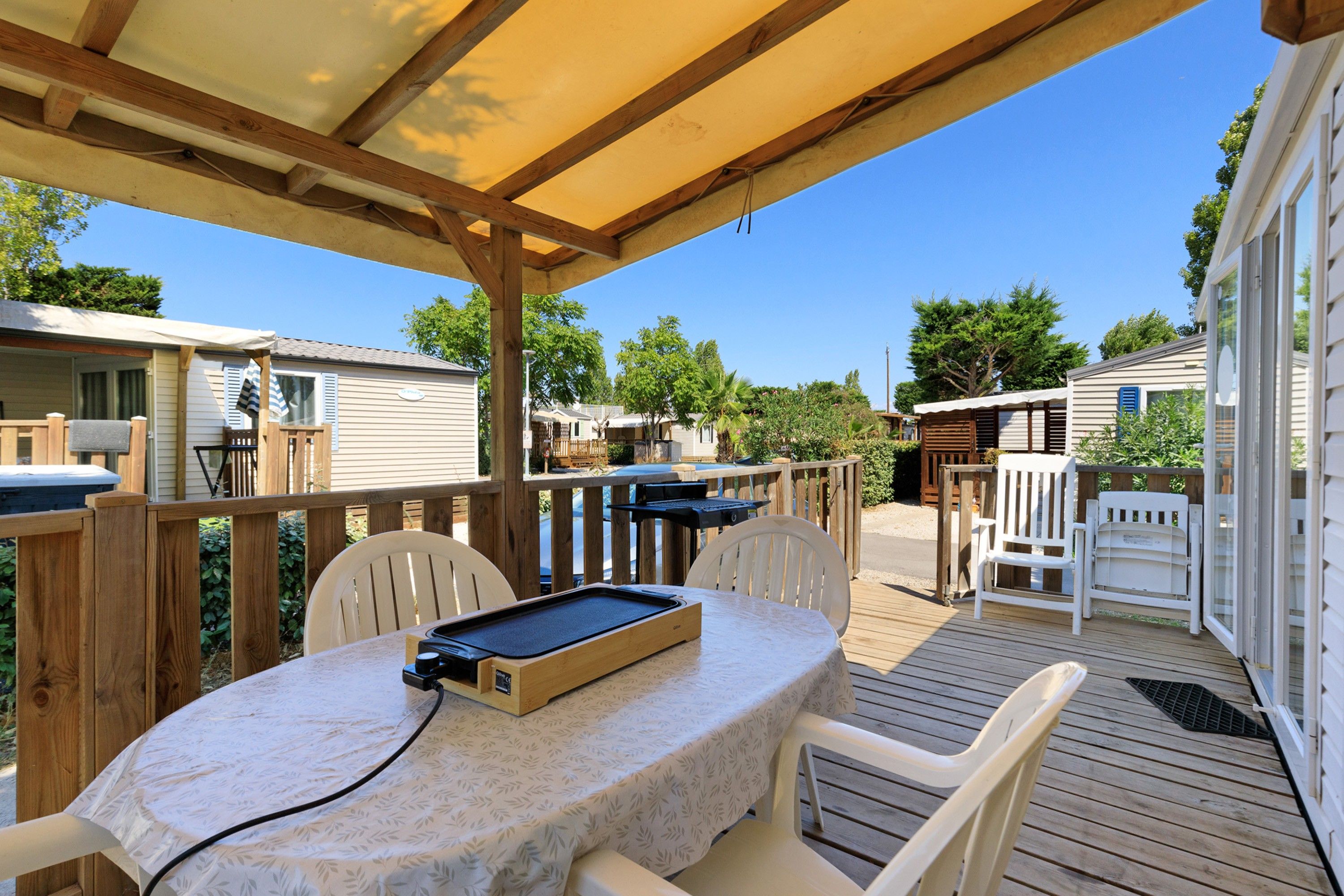 Une terrasse extérieure couverte, dotée d’une table et de chaises, entourée d’une plateforme en bois et d’une piscine.