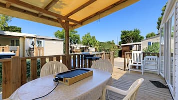 Une terrasse extérieure couverte, dotée d’une table et de chaises, entourée d’une plateforme en bois et d’une piscine.