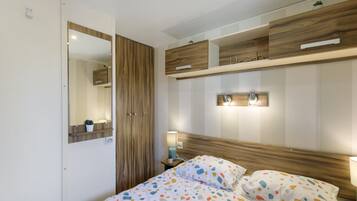 Une chambre à coucher comprenant un lit, une armoire en bois, un miroir, une table de chevet avec une lampe, et une étagère murale agrémentée d’objets décoratifs.