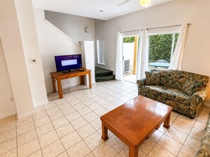 A living room with a wooden coffee table, a sofa, a TV on a stand, and a staircase leading to an outdoor area. - Your Next Adventure 3 (Kissimmee)