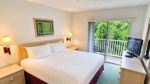 Habitación de hotel con cama, lámparas de noche, escritorio con televisor y balcón con vistas a zonas verdes.