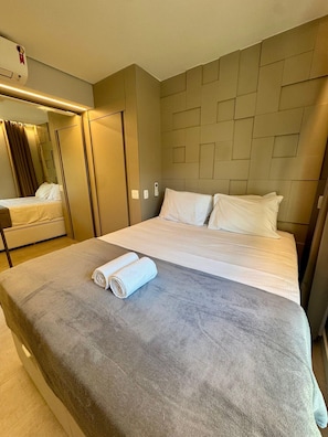 Quarto de hotel com uma cama, um espelho, um guarda-roupa e uma toalha sobre a cama.