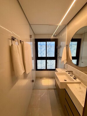 A modern bathroom with a glass shower enclosure, a large mirror, and a vanity with a sink. - CasaMirador Savassi (Belo Horizonte)