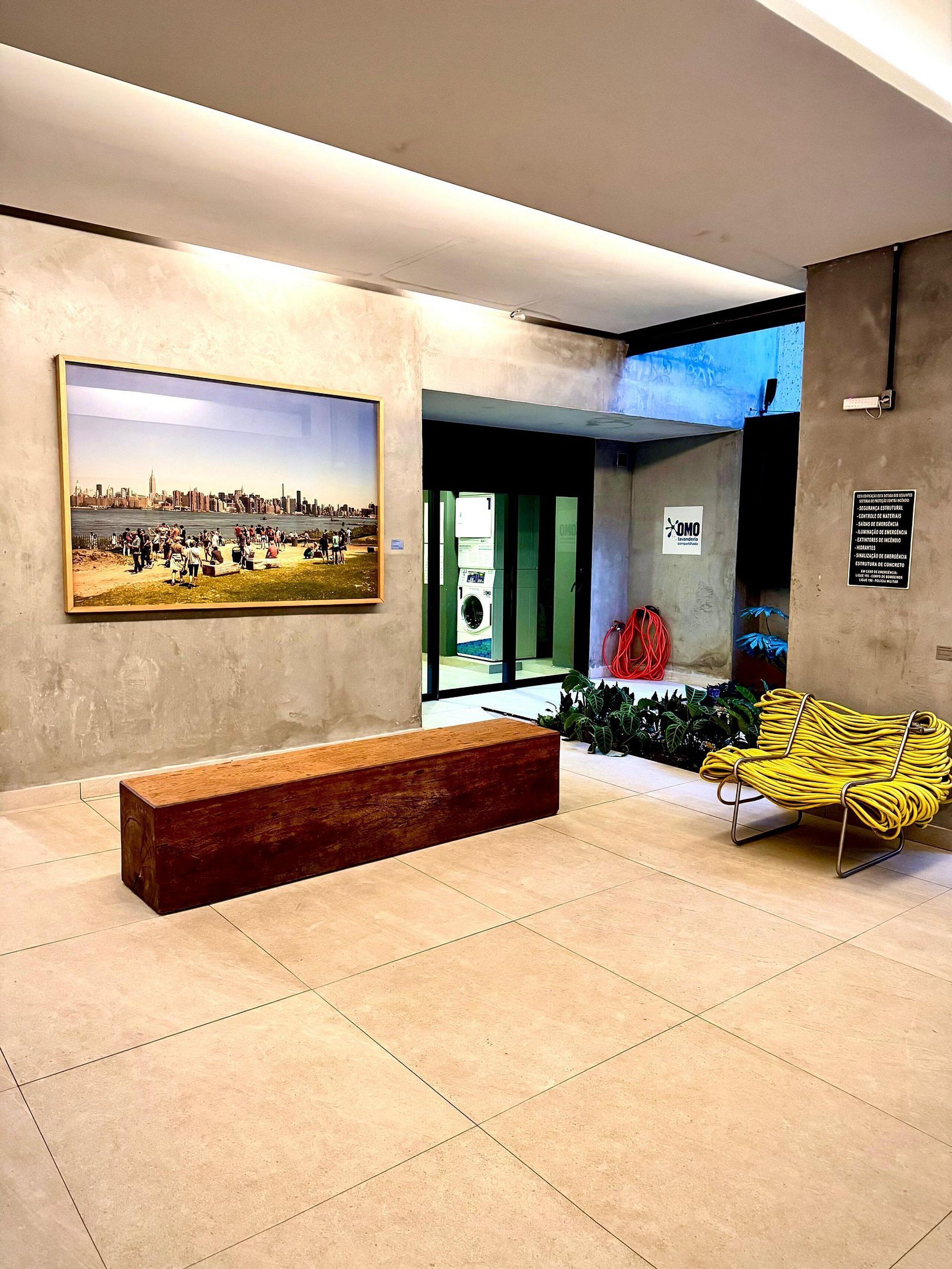 A lobby with a large painting, a bench, a yellow chair, and a green wall with a sign.