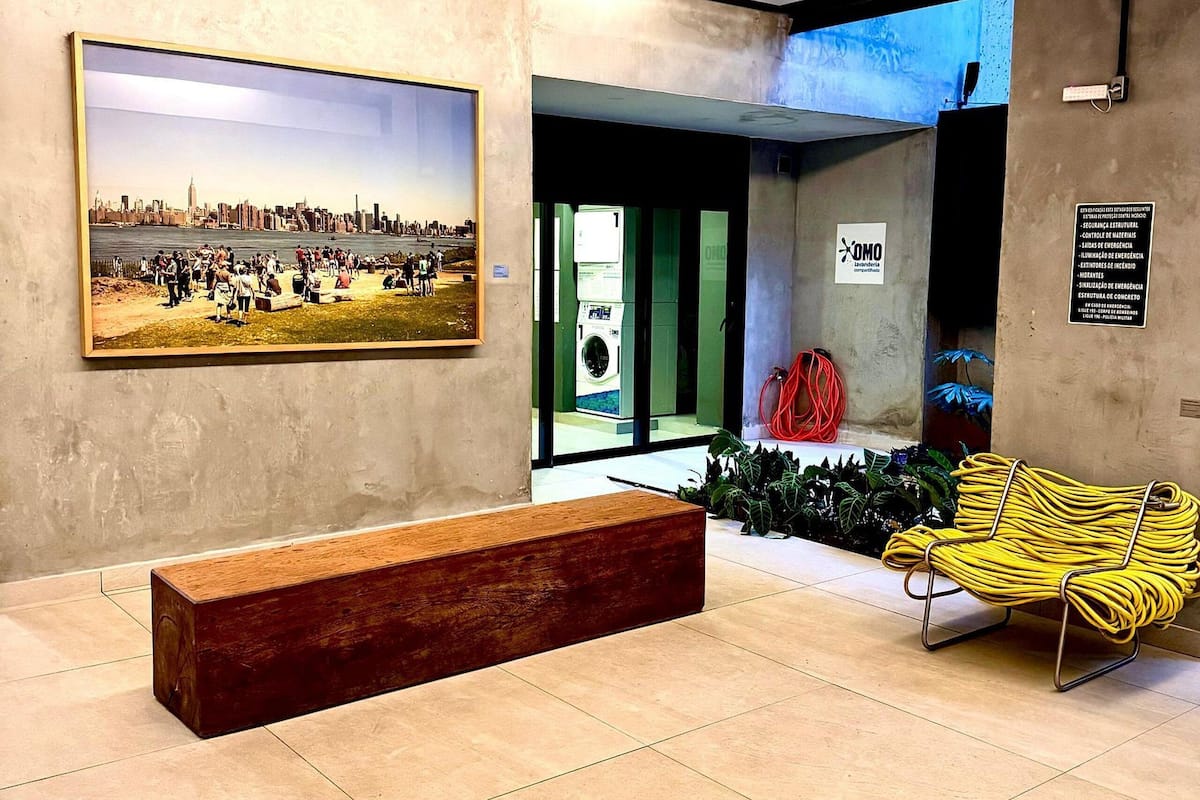 Um saguão com uma grande pintura, um banco, uma cadeira amarela e uma parede verde com uma placa.