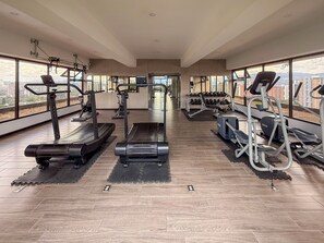 Un gimnasio amplio con cintas de correr, elípticas y estaciones de pesas, con ventanas grandes y un techo alto.