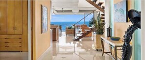 A spacious interior with a view of the ocean, a staircase leading to a balcony, and a dining area with a table and chairs. - Vista Bahía Penthouse - Private Rooftop Pool (Puerto Vallarta)