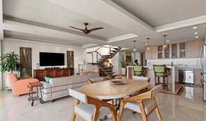 A modern living room with a sofa, a dining table, and a spiral staircase. - Vista Bahía Penthouse - Private Rooftop Pool (Puerto Vallarta)