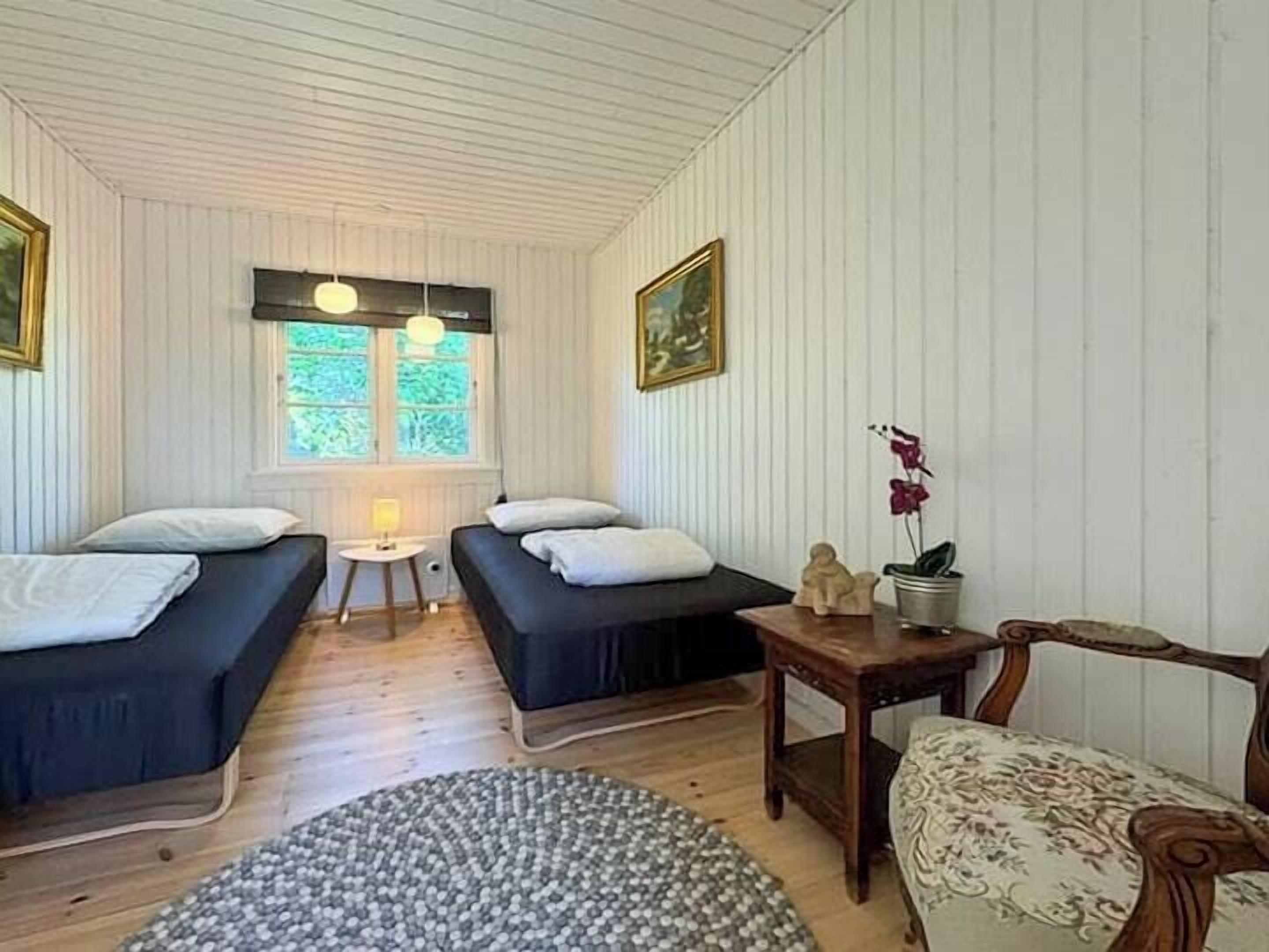 A room with two beds, a small table, a chair, a window with a view, and a painting on the wall.
