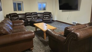 Una sala de estar con un sofá seccional, dos sillones, una mesa de centro y un televisor de pantalla plana montado en la pared.