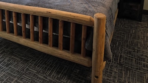 Una cama de madera con cabecera, dos lámparas de noche, un cuadro en la pared y una alfombra estampada.