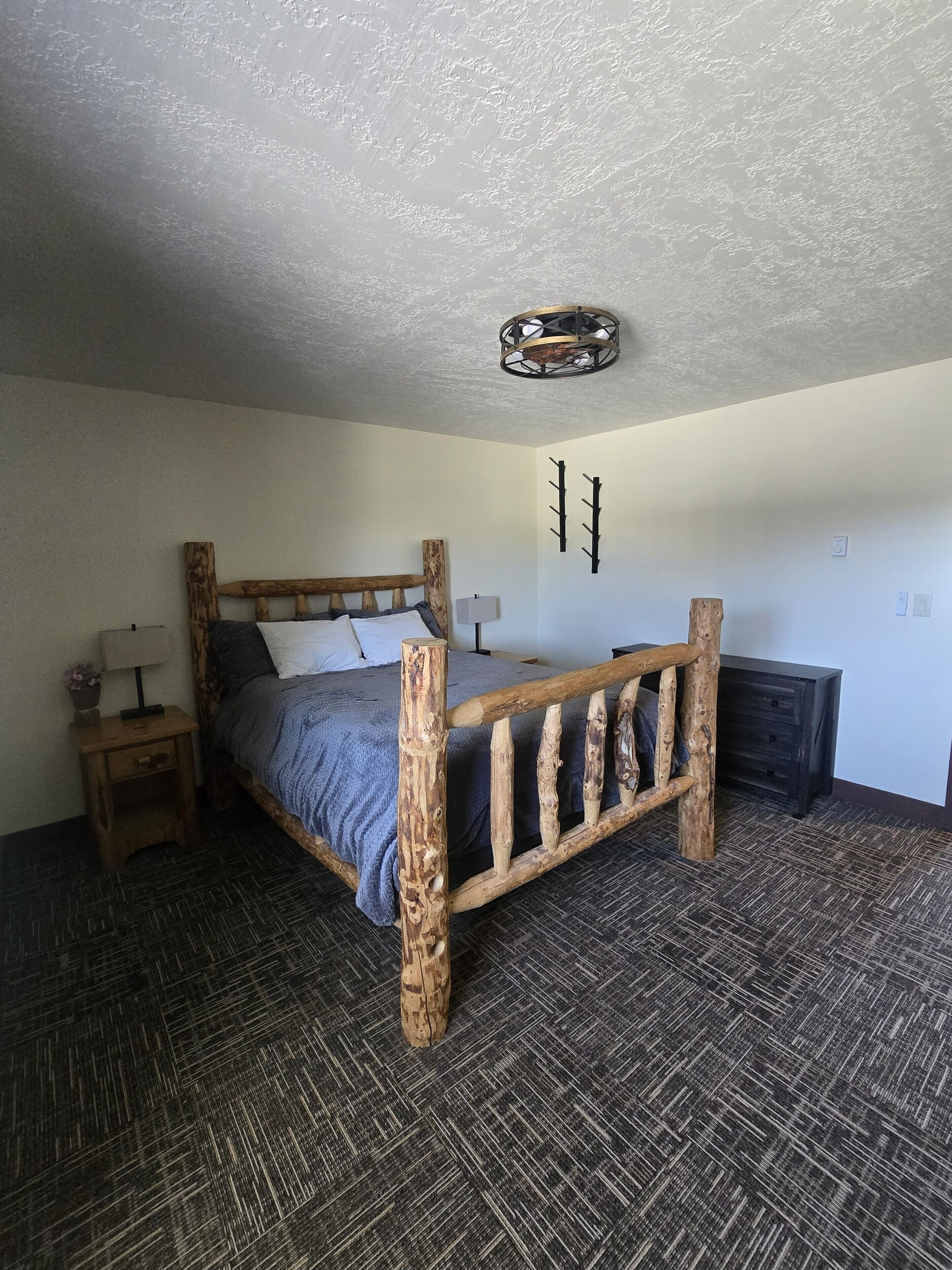 A bedroom with a wooden bed frame, a nightstand with a lamp, and a wall-mounted light fixture.