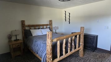 A bedroom with a wooden bed frame, a nightstand with a lamp, and a wall-mounted light fixture.