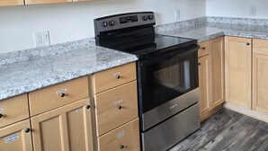 Una cocina con gabinetes de madera, estufa de acero inoxidable, encimeras de granito y piso de madera.