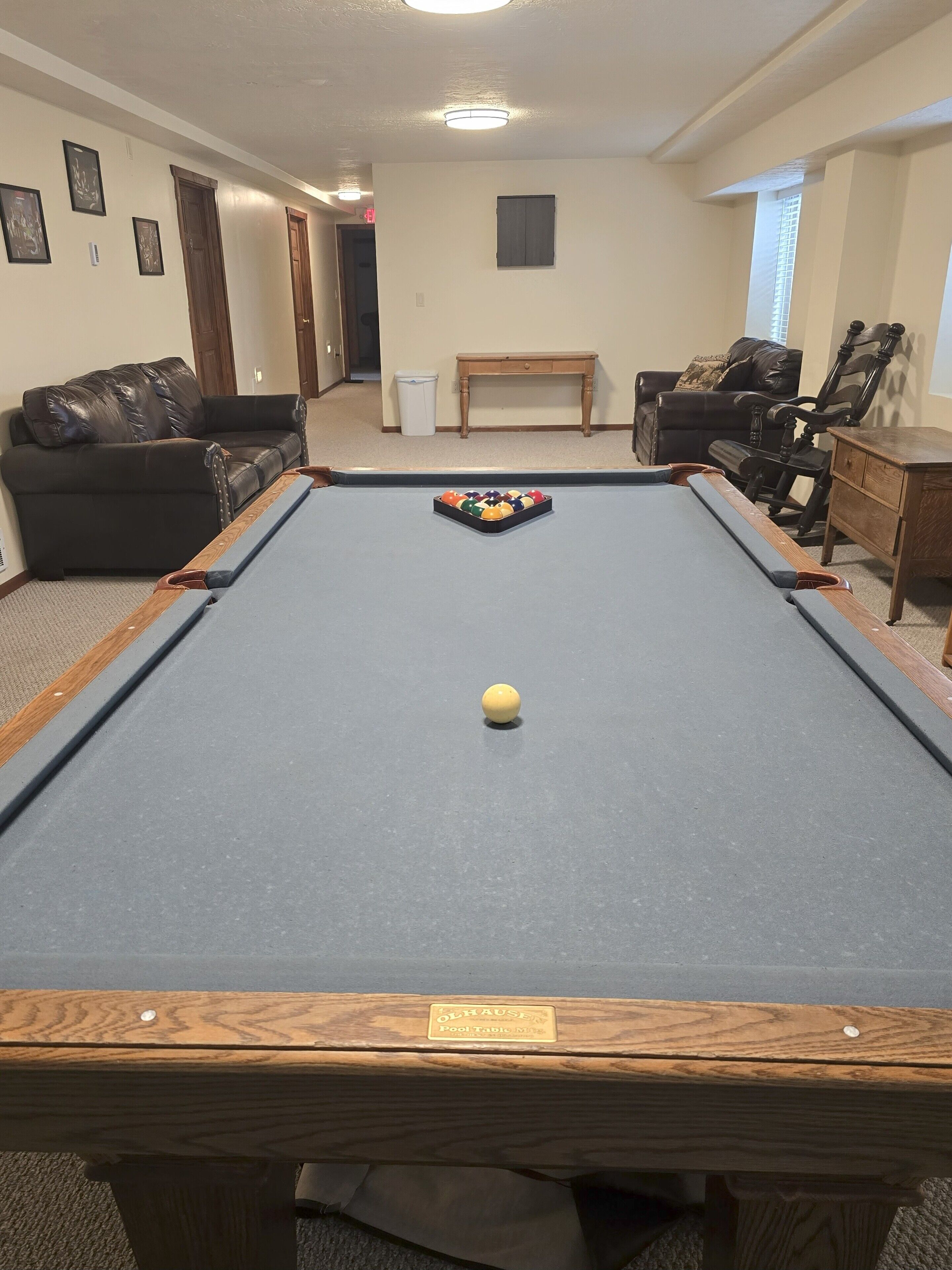 A pool table with a yellow ball in the center, surrounded by a leather sofa and a wooden chair.