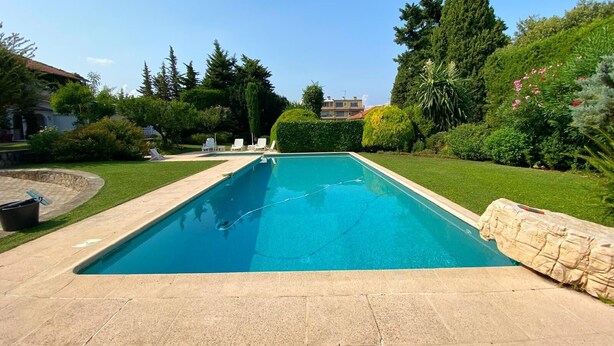 Una piscina rettangolare con bordo in pietra, circondata da un prato curato e diversi alberi.