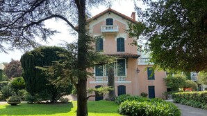 Un edificio su due piani con un balcone, immerso nel verde curato e con un vialetto lastricato.