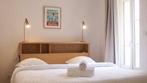 A neatly made bed with white linens, a wooden headboard, two bedside lamps, and a poster on the wall. - Agréable et Cosy - Suquet - proche des plages (Cannes)