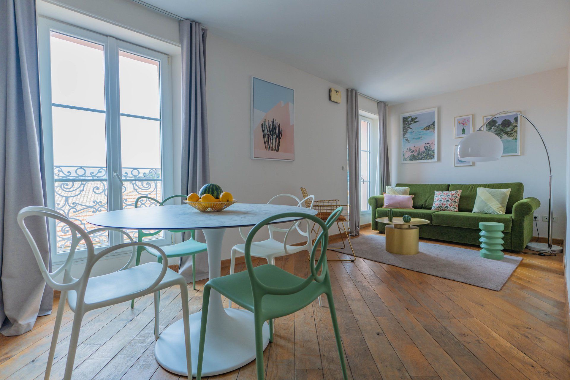 Una sala de estar moderna con una mesa redonda de comedor, sillas verdes y blancas, un sofá verde con cojines y una pequeña mesa auxiliar.