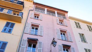 A pink building with a black door, white shutters, and a small balcony with metal railings. - Agréable et Cosy - Suquet - proche des plages (Cannes)