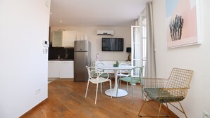 A compact kitchen with a refrigerator, a dining table with chairs, and a TV mounted on the wall. - Agréable et Cosy - Suquet - proche des plages (Cannes)
