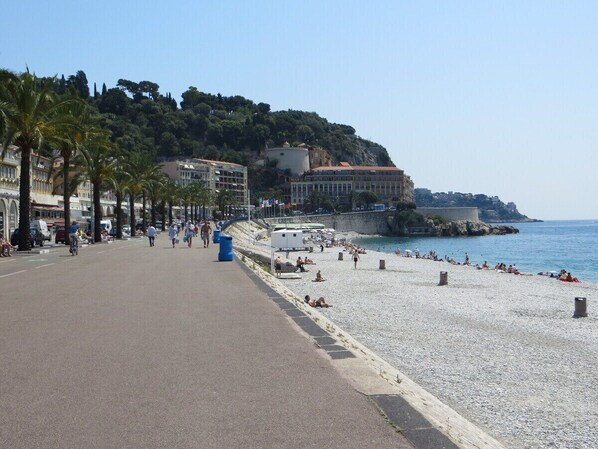 Eine Küstenpromenade mit Kiesstrand, einem Fußweg und Gebäuden im Hintergrund.