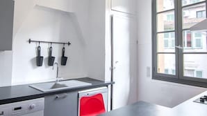 Une cuisine compacte équipée d’un lave-linge, d’un évier et d’une fenêtre donnant sur des immeubles.