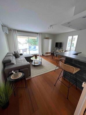 A modern living room with a sofa, coffee table, and chairs, a kitchen area with a bar, and large windows with a view. - Beautiful apartment - Centre (Cagnes-sur-Mer)