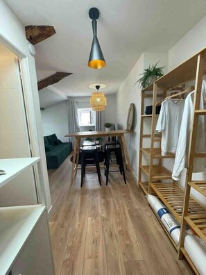 Ein kompakter Wohnbereich mit Holzboden, einer Essecke mit Tisch und Stühlen, einem Etagenbett mit Holzgestell und einer Pendelleuchte.