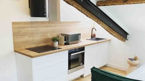 A compact kitchen with a microwave, oven, and sink, a green sofa, and a wooden ceiling beam. - Beautiful refurbished cozy apartment (Nice)