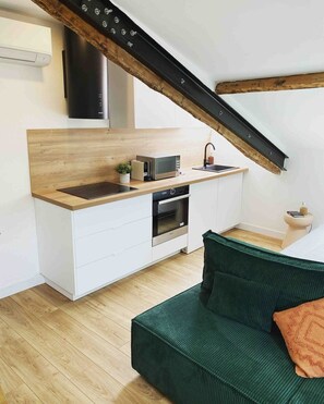 Eine kleine Küche mit Mikrowelle, Backofen und Spüle, ein grünes Sofa und ein Holzbalken an der Decke.