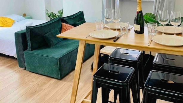 A cozy room with a loft bed, a green sofa, a dining table with chairs, and a hanging light fixture. - Beautiful refurbished cozy apartment (Nice)