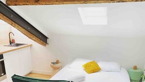 A loft-style bedroom with a green sofa, a bed with white and yellow pillows, a small bedside table, and a green nightstand. - Beautiful refurbished cozy apartment (Nice)