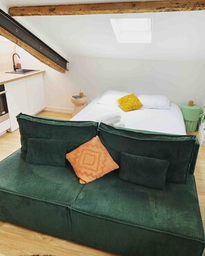 Ein Schlafzimmer im Loft-Stil mit einem grünen Sofa, einem Bett mit weißen und gelben Kissen, einem kleinen Nachttisch und einem Nachttisch in Grün.