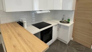 Eine moderne Küche mit weißen Schränken, einem schwarzen Herd, einer Holzausziehtafel, einer Spüle und einer Tür.