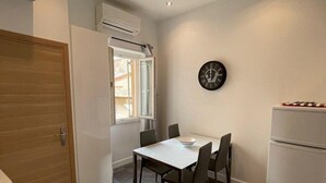 Eine kleine Küche mit Esstisch, Stühlen, einem Kühlschrank und einer Uhr an der Wand.