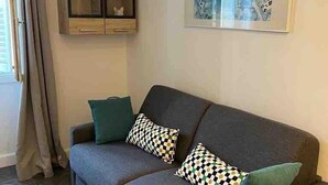 Ein Wohnzimmer mit grauem Sofa, gemusterten Kissen, einer Glaskabine und einem gerahmten Kunstwerk an der Wand.
