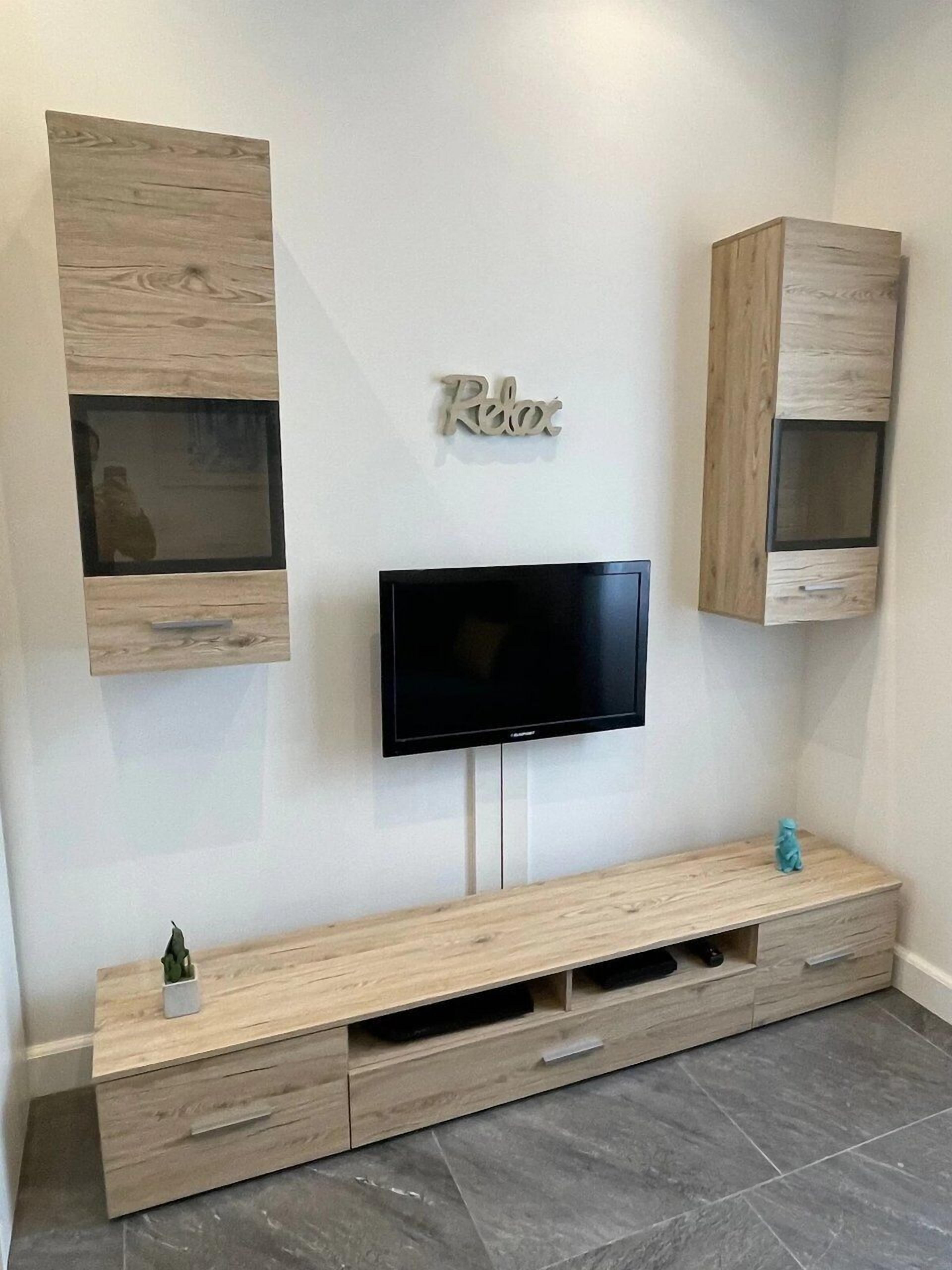 A modern living room with a flat-screen TV mounted on the wall, wooden cabinets, and a minimalist console table.