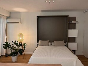Une chambre à coucher avec un lit, des lampes de chevet, une plante en pot et une étagère fixée au mur.