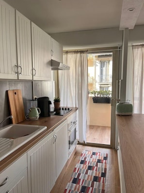 Une cuisine compacte avec des meubles blancs, un plan de travail en bois, une cuisinière à gaz, un évier et une petite fenêtre.