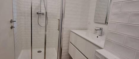 A modern bathroom with a glass-enclosed shower, white tiled walls, and a wooden floor.