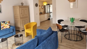 Uma sala de estar com sofá, poltrona e mesa de jantar com cadeiras.