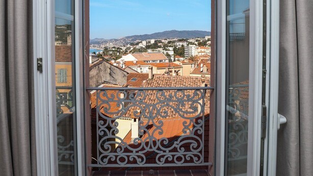 A balcony with a metal railing, a clear sky, and a view of a cityscape with buildings and hills. - Agréable et Cosy - Suquet - proche des plages (Cannes)
