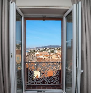 Un balcó amb barana metàl·lica, cel clar i vista de la ciutat amb edificis i turons.